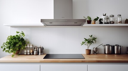 Silver cooker hood in minimal white kitchen interior with plant on wooden countertop. Real photo