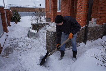 A man cleans snow in the winter in the courtyard of the house.