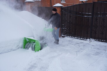 A man cleans snow in the winter in the courtyard of the house,  man cleaning snow with a snow blower