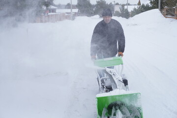 A man cleans snow in the winter in the courtyard of the house,  man cleaning snow with a snow blower