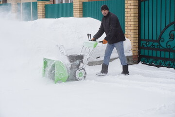A man cleans snow in the winter in the courtyard of the house,  man cleaning snow with a snow blower