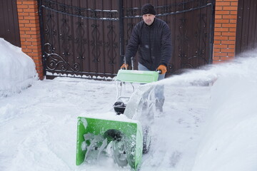 A man cleans snow in the winter in the courtyard of the house,  man cleaning snow with a snow blower