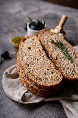 Freshly baked sourdough bread from whole grain flour and pumpkin seeds on a grid, olive oil and black olive on a rustic wooden table. Artisan bread.
