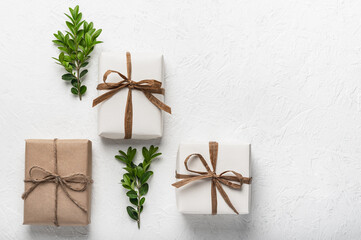Three craft gift boxes on a white background and green boxwood branches. The concept of holidays and DIY gifts. Postcard, mock-up.