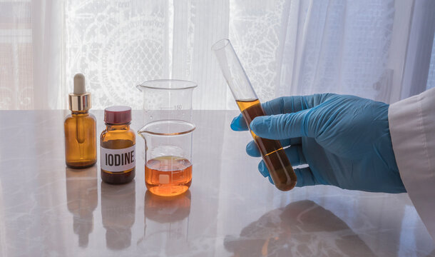 glass tube with iodine. hand with glove holding a glass jar with the substance iodine. lugol