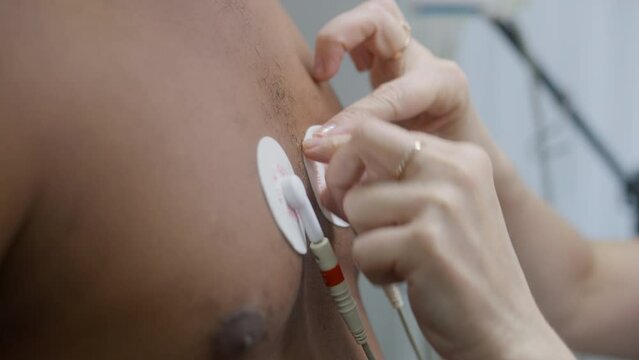Female doctor puts sensors for holter monitoring on patient with heart disease. African American man during functional rehabilitation in cardiology room. Electrocardiography in modern clinic. Close up