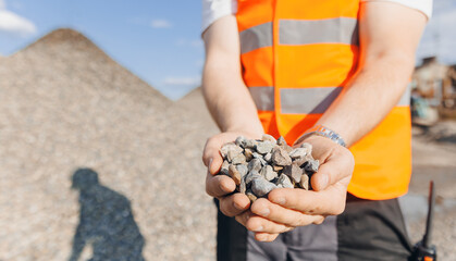 Worker engineer hold gravel in hand, checks quality at sand quarry. Industrial construction site concept - obrazy, fototapety, plakaty