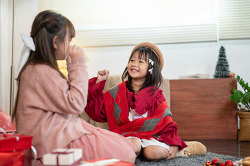 Two cheerful young Asian girls are enjoying playing rock-paper-scissors on Christmas night.