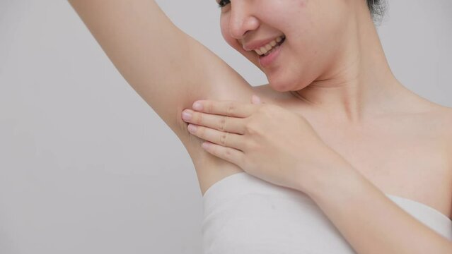 Close-up of beautiful Asian woman applying cream or lotion on armpits to treat skin