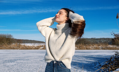 snowy winter landscape of a frozen lake, with attractive, young, sexy, brunette woman, holding her head in her hands and relaxed enjoying the vacation winter sun