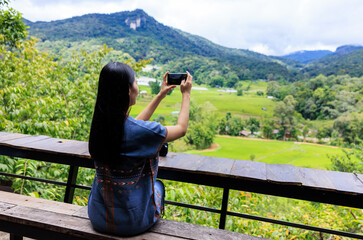 Fototapeta na wymiar young girl sitting on balcony and used the phone to take pictures of the mountain view,