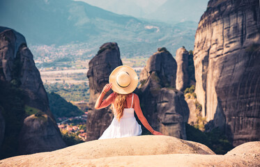 Young woman in white dress sitting on cliff looking at Meteor mountain landscape in Greece- Meteora