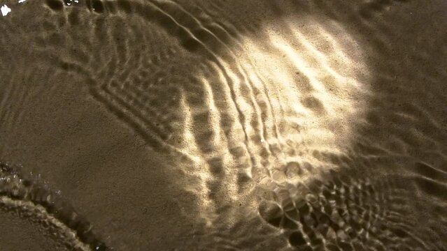 Water surface ripples and splash, round bright light and shadow on sand texture
