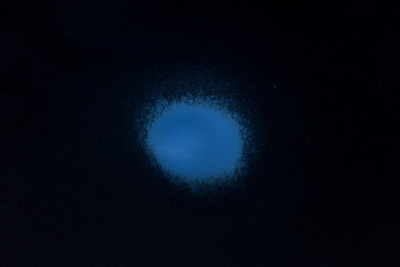 a blue spray paint stain on a black paper background