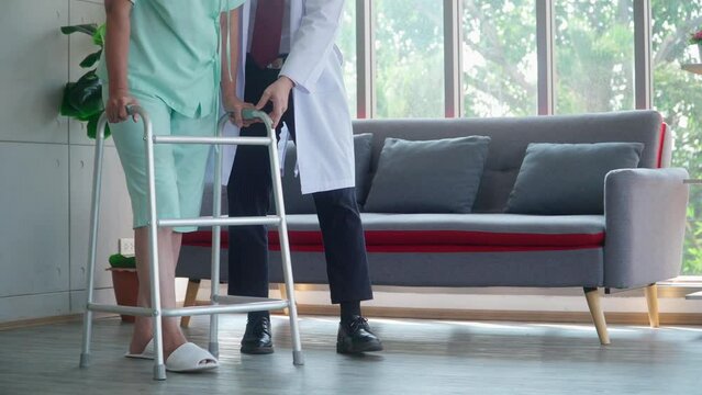 A doctor helping an elderly patient walks by using a walker.