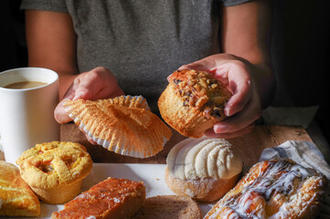 Woman's hand taking a piece of Mexican sweet bread from a white plate on a wooden table. Concept of hands handling food, holding a Mexican nut muffin, front view