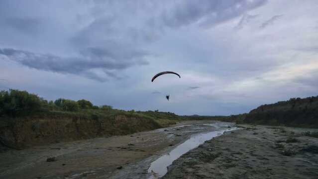 Paragliders flying over drying up desert river - steady cam, wide shot