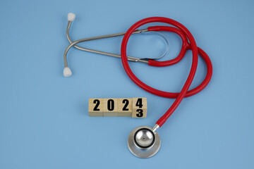 Health care in year 2024. Red stethoscope and numbers 2023 and 2024 on wooden cubes on blue. 