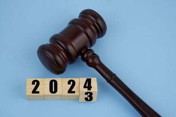 Gavel and numbers 2023 and 2024 on wooden cubes on blue background. New laws in year 2024.