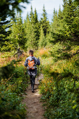 Girl in sports outfit with backpack on her back walking along a path in the forest, back view of a sporty man, hiking in the mountains, hiking.