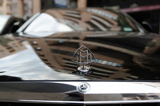 Yerevan Armenia August 4 2023: Closeup emblem logo on front of brand Mercedes Maybach S500 dark  car, sky and city reflection on car bonnet