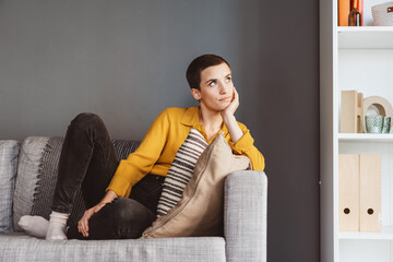 Young Modern Woman with Short Hair Lying on Sofa, Gazing Thoughtfully Upwards
