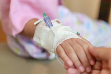 Mother holding child hand with saline IV solution in hospital