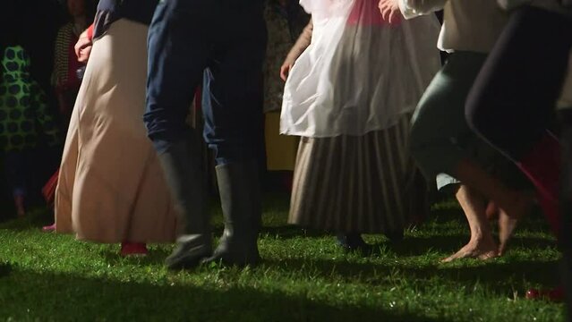 hand held medium shot of people dancing in the midsummer night in the middle of the meadow in folk costumes