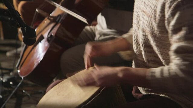 hand held close up shot of a small group of musicians playing cello and percussion drums with hands