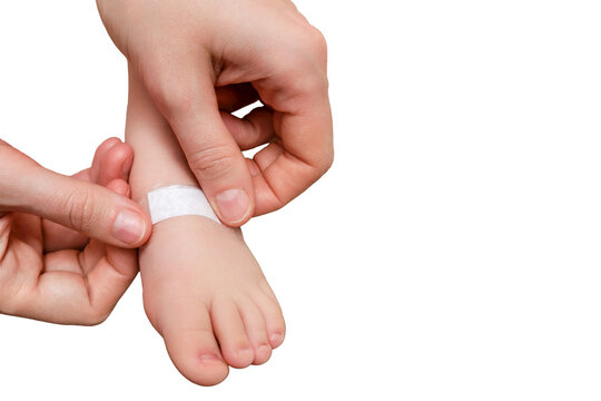 Mother woman sticks a medical adhesive plaster on the toddler baby leg, isolated on a white background. Mom s hand with sticky wound protection tape and child foot. Kid aged one year and three months