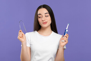 Woman with tongue cleaner and electric toothbrush on violet background