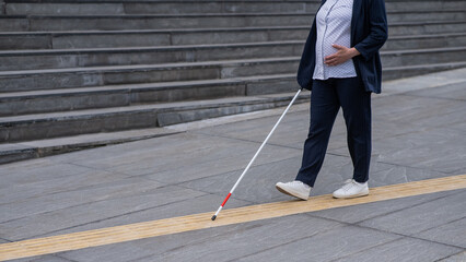 Blind pregnant businesswoman walking along tactile tiles with a cane. 