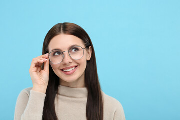 Smiling woman in stylish eyeglasses on light blue background. Space for text