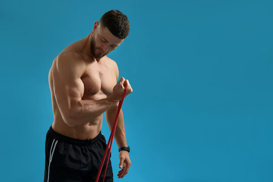 Muscular man exercising with elastic resistance band on light blue background. Space for text