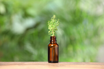 Bottle with essential oil and thyme on wooden table against blurred green background