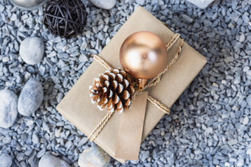 Fototapeta na wymiar Gift box with gold christmas ball and pine cone on stone background