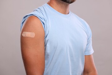 Man with sticking plaster on arm after vaccination against light grey background, closeup