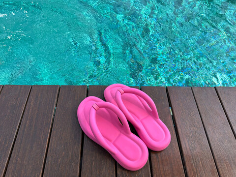 Clear rippled water in swimming pool and pink flip-flops on wooden deck outdoors, closeup