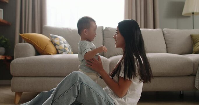 Mother And Child Playing At Home. Cinematic, Chinese, Japanese, Korean, Asian. Happy Loving Millennial Mom Sitting On Floor With Her Little Boy. Relaxed Happy Mother And Baby Spending Time Together