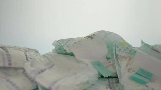 A man takes a baby diaper from a stack of scattered baby diapers on a white background. Copy space for text. Slow motion