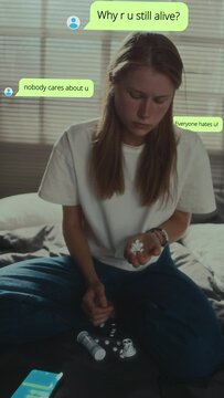 Vertical shot of depressed girl sitting on bed at home, holding handful of pills and planning suicide cause of cyberbullying. CG animated text messages popped up around her