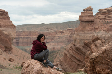 Fototapeta na wymiar A young woman sits on a rock in the Central Asian Canyon, Charyn, Kazakhstan