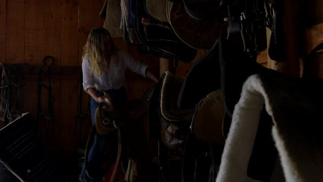 Young woman putting away a saddle and storing it