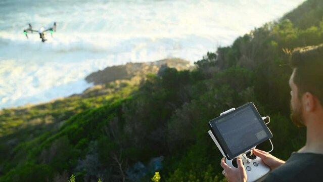 Hands, tablet and a man flying a drone over the ocean in nature for video footage during summer. Beach, sea and waves with a person using a remote to control technology on the coast by the water