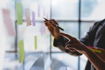 Team business people writing planning and brainstorming putting sticky notes on glass wall in the...