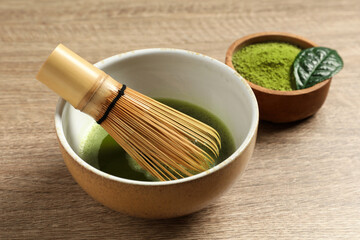 Cup of fresh matcha tea with bamboo whisk and green powder on wooden table