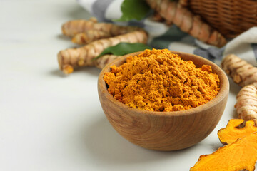Aromatic turmeric powder and raw roots on white table, closeup. Space for text