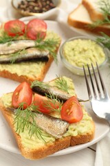 Delicious sandwiches with sprats, tomatoes, dill and avocado puree served on white wooden table