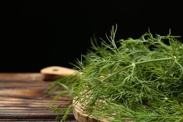 Naklejka premium Board with fresh green dill on wooden table against black background, closeup. Space for text