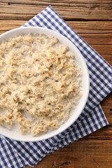 Tasty boiled oatmeal in bowl on wooden table, top view